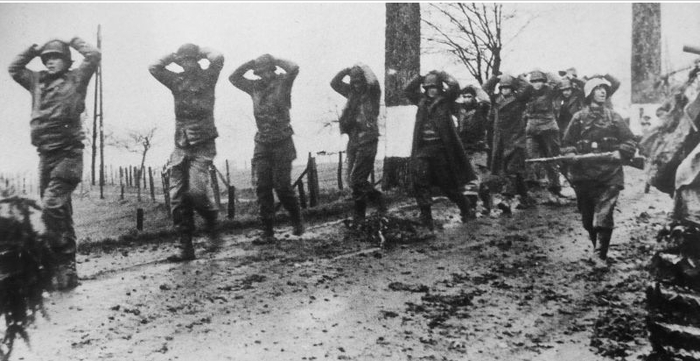 Немецкий солдат конвоирует американских военнопленных по дороге в Арденнах